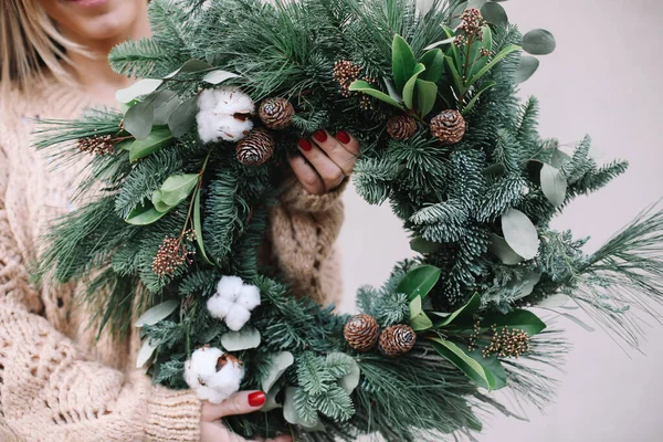 Christmas decorations. Christmas wreath. Florist making Christmas wreath. View of female hands holding a wreath.