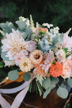 Gelinin pembe, kırmızı ve turuncu çiçekli düğün buketi ahşap masada yatıyor.