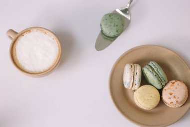 Beyaz arka planda kahverengi tabakta ev yapımı renkli badem kurabiyeleri. Bir fincan kahve. Çiçek..