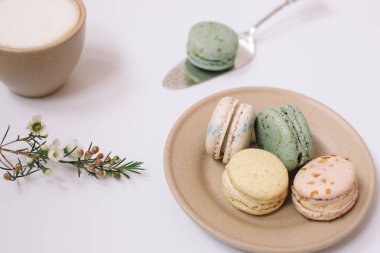 Beyaz arka planda kahverengi tabakta ev yapımı renkli badem kurabiyeleri. Bir fincan kahve. Çiçek..