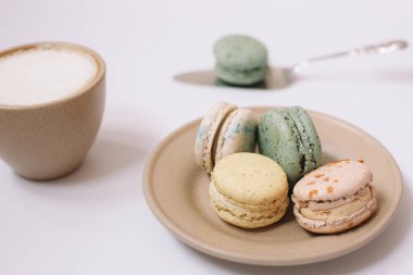 Beyaz arka planda kahverengi tabakta ev yapımı renkli badem kurabiyeleri. Bir fincan kahve. Çiçek..