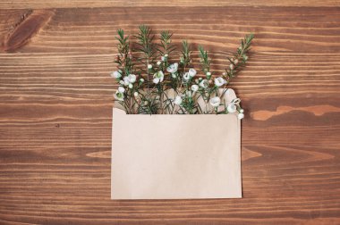 Açılmış kağıt zarf bahar çiçekleriyle dolu kahverengi ahşap arka planda yatıyor.