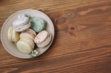 Kahverengi ahşap arka plandaki bej tabakta renkli ev yapımı badem kurabiyeleri var. Desen.