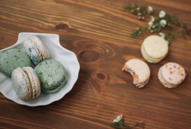 Ev yapımı badem kurabiyeleri ahşap arka plandaki beyaz tabakta duruyor. Ahşap arka planda çiçekli sarı ve bej badem kurabiyeleri var..