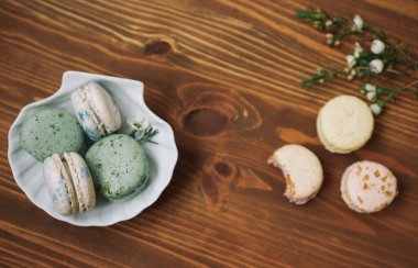 Ev yapımı badem kurabiyeleri ahşap arka plandaki beyaz tabakta duruyor. Ahşap arka planda çiçekli sarı ve bej badem kurabiyeleri var..