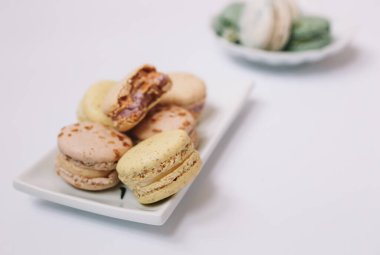 Ev yapımı badem kurabiyeleri beyaz tabakta, beyaz arka planda, yeşil ve beyaz makaronları tabakta duruyor.