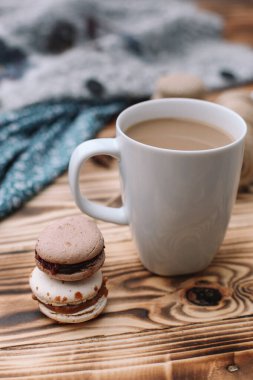 İki ev yapımı renkli badem kurabiyesi kahverengi ahşap masada bir fincan kahveyle birlikte yatıyor. Bir fincan kahve. Renkli doku.