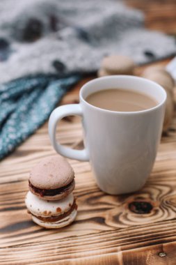 İki ev yapımı renkli badem kurabiyesi kahverengi ahşap masada bir fincan kahveyle birlikte yatıyor. Bir fincan kahve. Renkli doku.