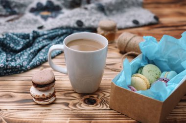 İki ev yapımı renkli badem kurabiyesi kahverengi ahşap masada bir fincan kahveyle birlikte yatıyor. Bir fincan kahve. Renkli doku.