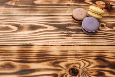 Üç tane ev yapımı renkli badem kurabiyesi kahverengi ahşap masanın üzerinde, kahve fincanı ve yazı için kullanılacak yer var. Renkler.