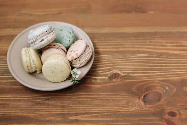 Kahverengi ahşap arka plandaki bej tabakta renkli ev yapımı badem kurabiyeleri var. Desen.