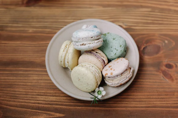 Kahverengi ahşap arka plandaki bej tabakta renkli ev yapımı badem kurabiyeleri var. Desen.