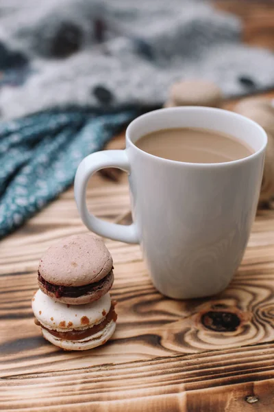 İki ev yapımı renkli badem kurabiyesi kahverengi ahşap masada bir fincan kahveyle birlikte yatıyor. Bir fincan kahve. Renkli doku.