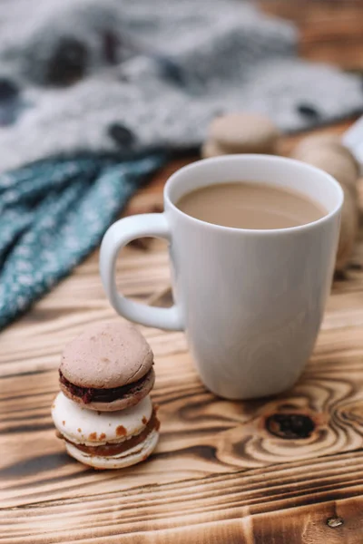 İki ev yapımı renkli badem kurabiyesi kahverengi ahşap masada bir fincan kahveyle birlikte yatıyor. Bir fincan kahve. Renkli doku.