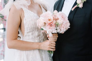 Gelin ve damat ellerinde pembe güller ve şakayıklıklarla düğün buketi tutuyorlar. Düğün günü..