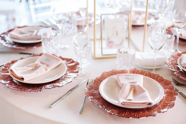 Wedding. Banquet. Glass table with pink and white flowers and red and white plates on it, served with cutlery, flowers and crockery.