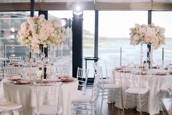 結婚式 宴会だ 椅子とお客様のための丸いテーブル カトラリー 花や食器で提供し ピンクと白の花と赤のプレートとテーブルクロスで覆われて ストックフォト