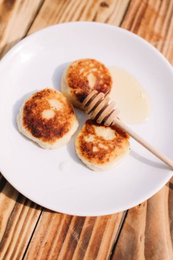 Lezzetli üç süzme peynirli krep. Beyaz tabağın üzerinde bal var. Ahşap masa zemininde çiçek açan bir ağacın dalı var. Peynirli börek..