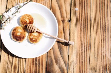Lezzetli üç süzme peynirli krep. Beyaz tabağın üzerinde bal var. Ahşap masa zemininde çiçek açan bir ağacın dalı ve yazı için bir yer var. Peynirli börek..