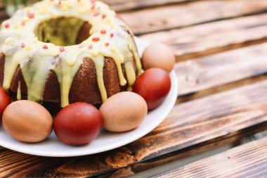 Yumurtaların etrafında bir gülümsemeyle kırmızı paskalya yumurtası ve ahşap arka planda beyaz tabakta paskalya pastası.