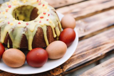 Yumurtaların etrafında bir gülümsemeyle kırmızı paskalya yumurtası ve ahşap arka planda beyaz tabakta paskalya pastası.
