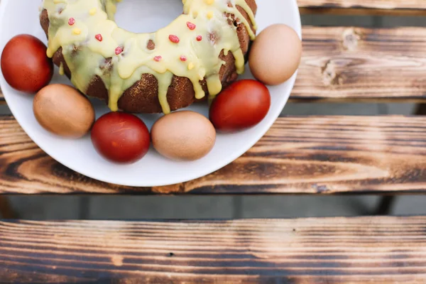 Red easter egg with a smile around eggs and Easter cake in the white plate on the wooden background