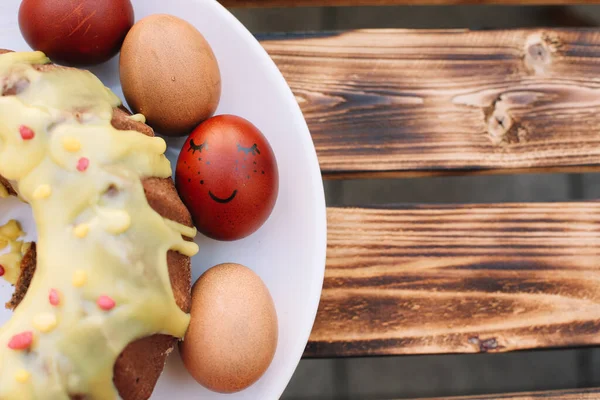 木製の背景に白いプレートに卵とイースターケーキの周りの笑顔で赤いイースターの卵 — ストック写真