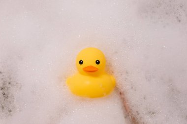 Banyoda köpüklü sarı plastik ördek tutan kız.