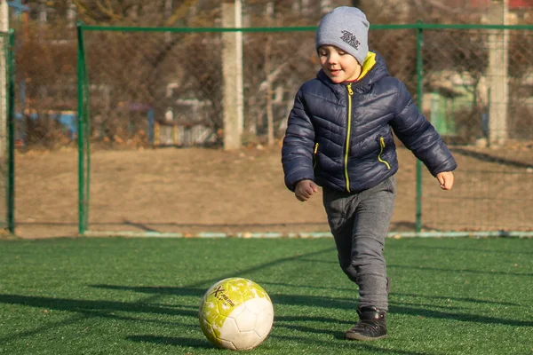 Egy 4 éves fiú focizik egy labdával egy műgyepen. — Stock Fotó