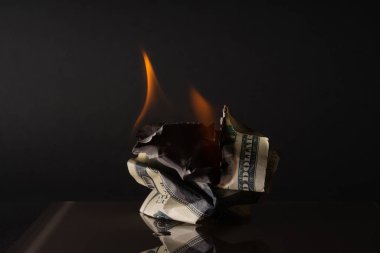 Yüz dolarlık banknot yakıyor. Karanlık bir arka planda. Yaratıcı boşluk