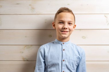 10 yaşında, mavi tişörtlü bir çocuk hafif bir tahta üzerinde gülümsüyor.