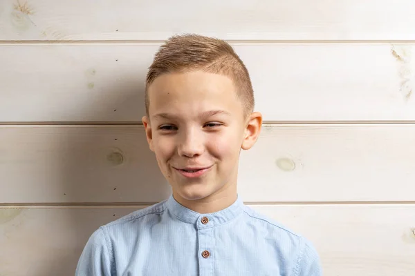 Ένα αγόρι 10 ετών με μπλε πουκάμισο χαμογελά σε ένα ανοιχτό ξύλινο b — Φωτογραφία Αρχείου