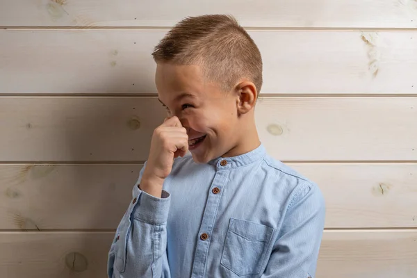 En 10-årig pojke i blå skjorta ler på en lätt trä baksida — Stockfoto