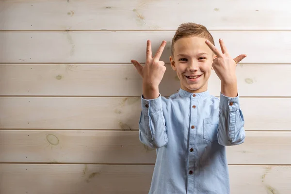 En pojke på 10 år i en blå skjorta ler på ett ljust trä b — Stockfoto