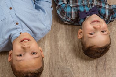 Mavi klepi tişörtlü 4 yaşındaki bir çocuk açık tahta arka planda ağlıyor ve 10 yaşındaki ağabeyi yerde yatıyor ve eğleniyor..