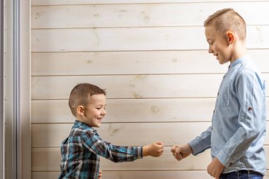 Mavi klepsi gömlekli 4 yaşındaki bir çocuk, tahta bir arka planda ağlarken, 10 yaşındaki ağabeyi ayakta duruyor..