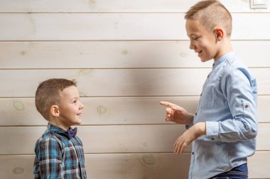 Mavi klepsi gömlekli 4 yaşındaki bir çocuk, tahta bir arka planda ağlarken, 10 yaşındaki ağabeyi ayakta duruyor..