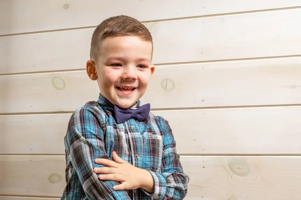 En 4 år gammal pojke i en blå prästskjorta gråter på en ljus trä bakgrund. — Stockfoto
