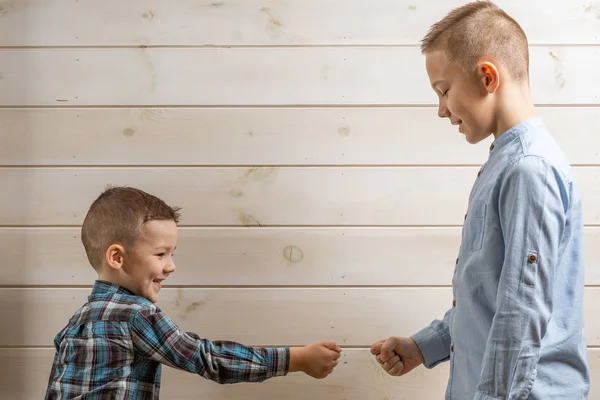 A 4-year-old boy in a blue klepy shirt cries on a light wooden background and his brother, 10 years old, is standing.