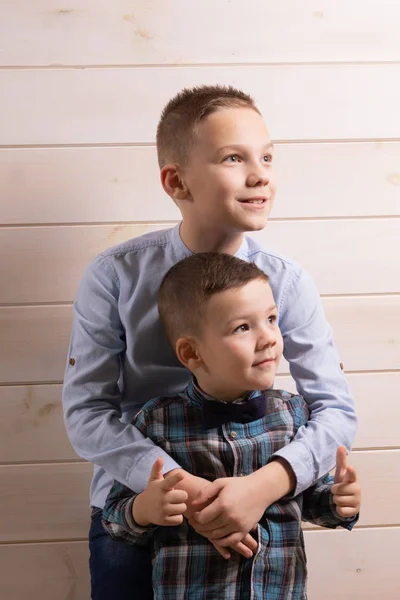 En 4-årig pojke i en blå kletig skjorta gråter på en ljus trä bakgrund och hans bror, 10 år gammal, står. — Stockfoto