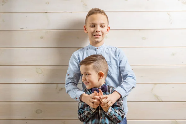 Un garçon de 4 ans portant une chemise bleue pleure sur un fond de bois clair et son frère, âgé de 10 ans, se tient debout. . — Photo