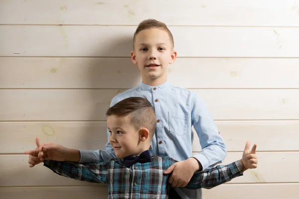 A 4-year-old boy in a blue klepy shirt cries on a light wooden background and his brother, 10 years old, is standing.