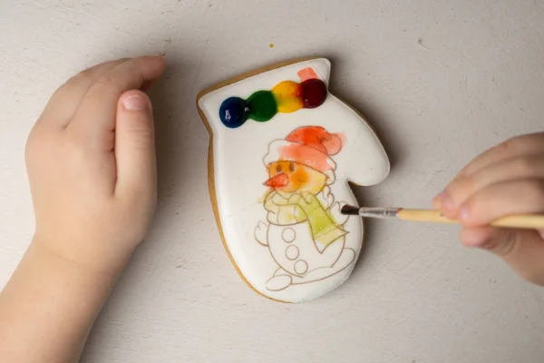 Ein 4-jähriger Junge bemalt einen Keks mit Lebensmittelfarben in einer Glasur. — Stockfoto