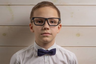 10 yıllık gözlüklü bir çocuk ahşap bir duvarın arkasında.