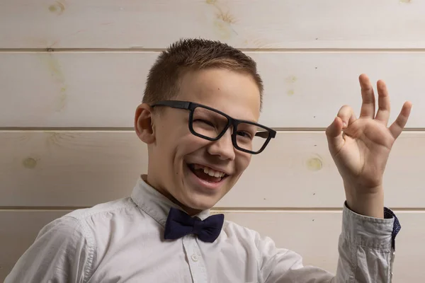 En 10 år gammal pojke med glasögon ler och visar ok symbolen på en trävägg bakgrund. — Stockfoto