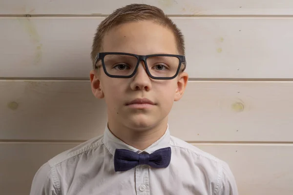 En pojke på 10 år i glasögon på en bakgrund av en trävägg. — Stockfoto