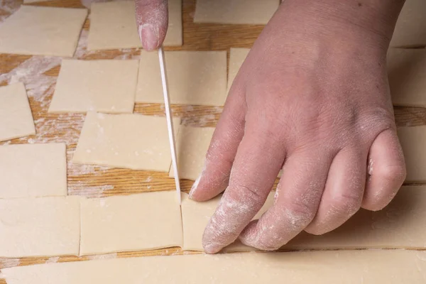 Eine Frau schneidet den Teig mit einem weißen Keramikmesser in Quadrate. — Stockfoto