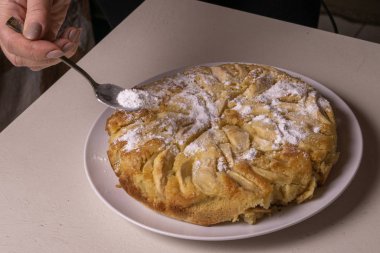 Kadın elleri pudra şekerli elmalı turta serpiyor..