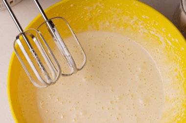 Bir kadın, bir turtanın malzemelerini sarı bir kaseyle karıştırır.