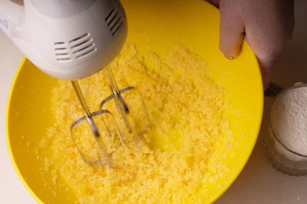 Una donna mescola gli ingredienti per una torta in una ciotola gialla con un — Foto Stock